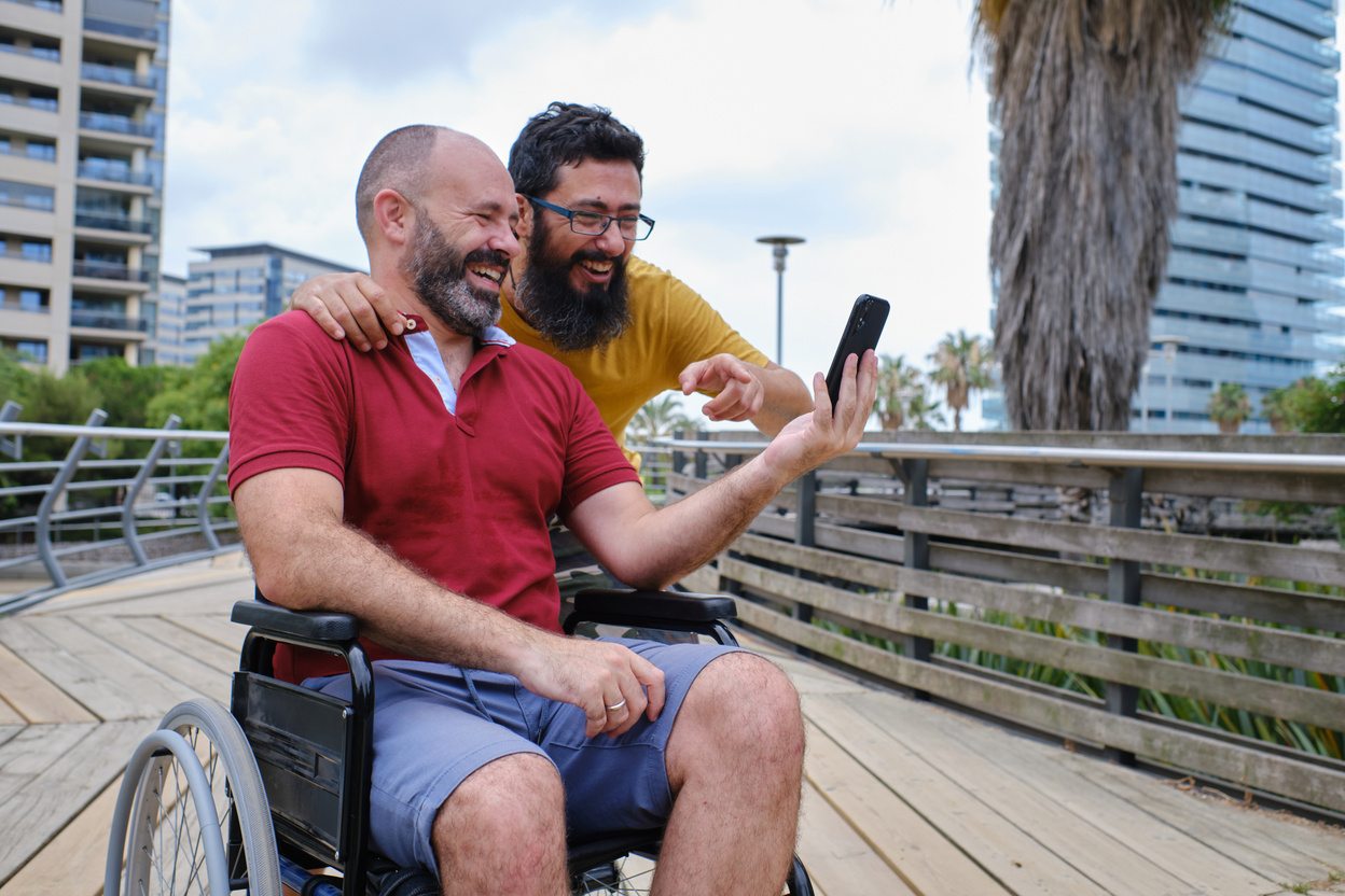 Disabled Man in a Wheelchair Showing His Phone to Friend
